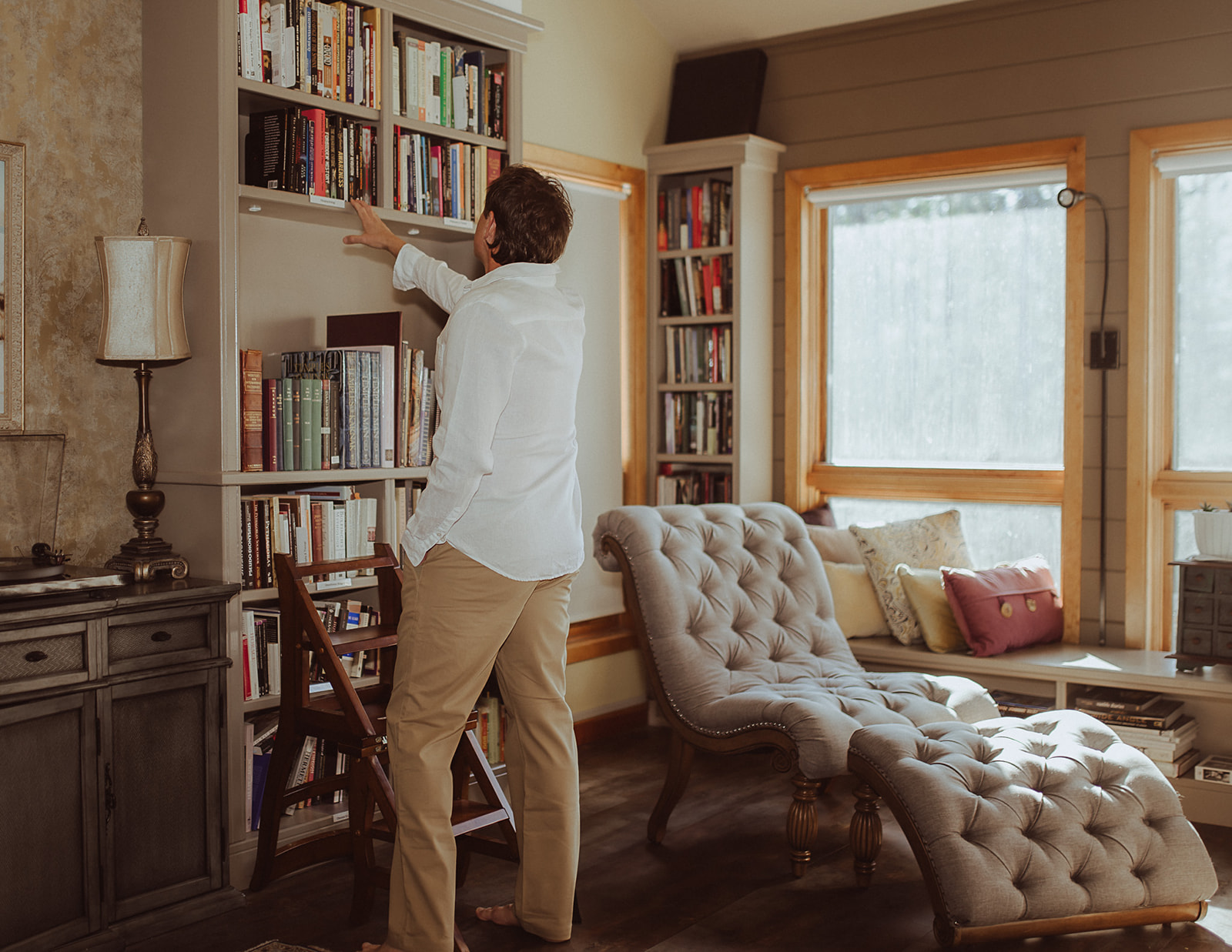 A man in a white shirt and khakis looks at some books on a shelf after visiting boutique hotels in Montana