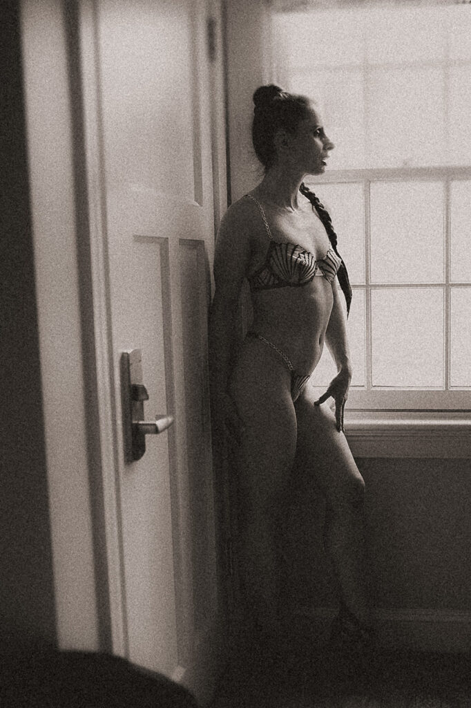 A woman in lingerie stands in a window in heels looking out