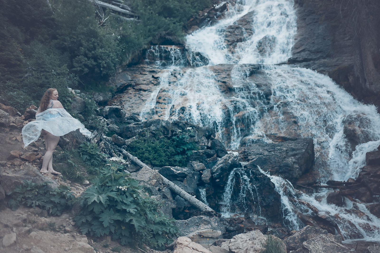 A woman explores a waterfall and climbs the trail in a white lace gown