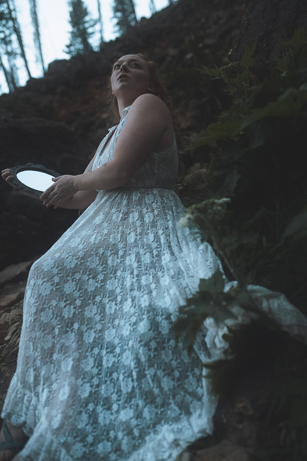 A woman looks over her shoulder while sitting in a forest with a hand mirror after some hot yoga in Missoula