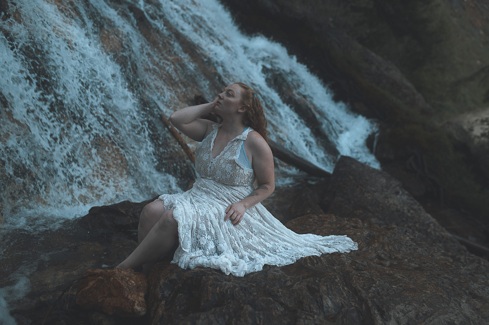 A woman in a white lace gown sits on the edge of a waterfall after some hot yoga in Missoula