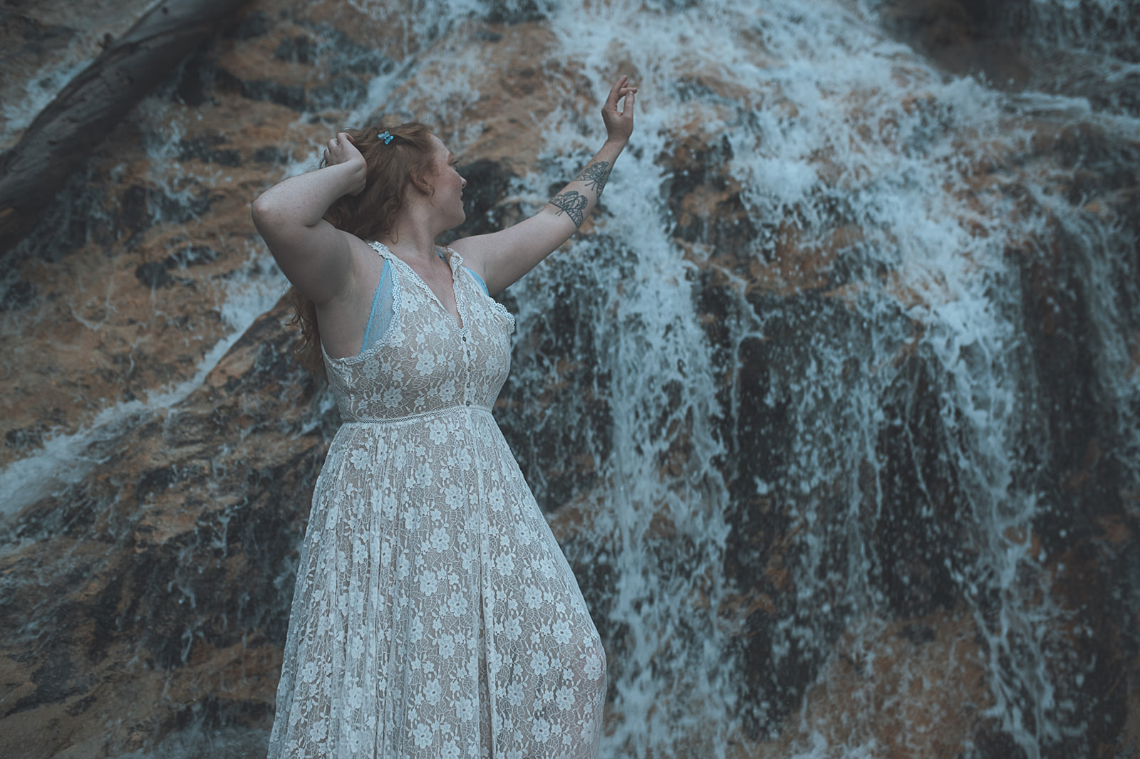 A red hair woman reaches for a waterfall in a white lace dress after visiting nail salons in Kalispell, MT