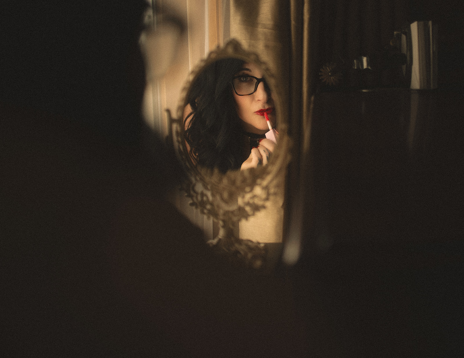 A woman with black hair applies red lipstick in an antique mirror
