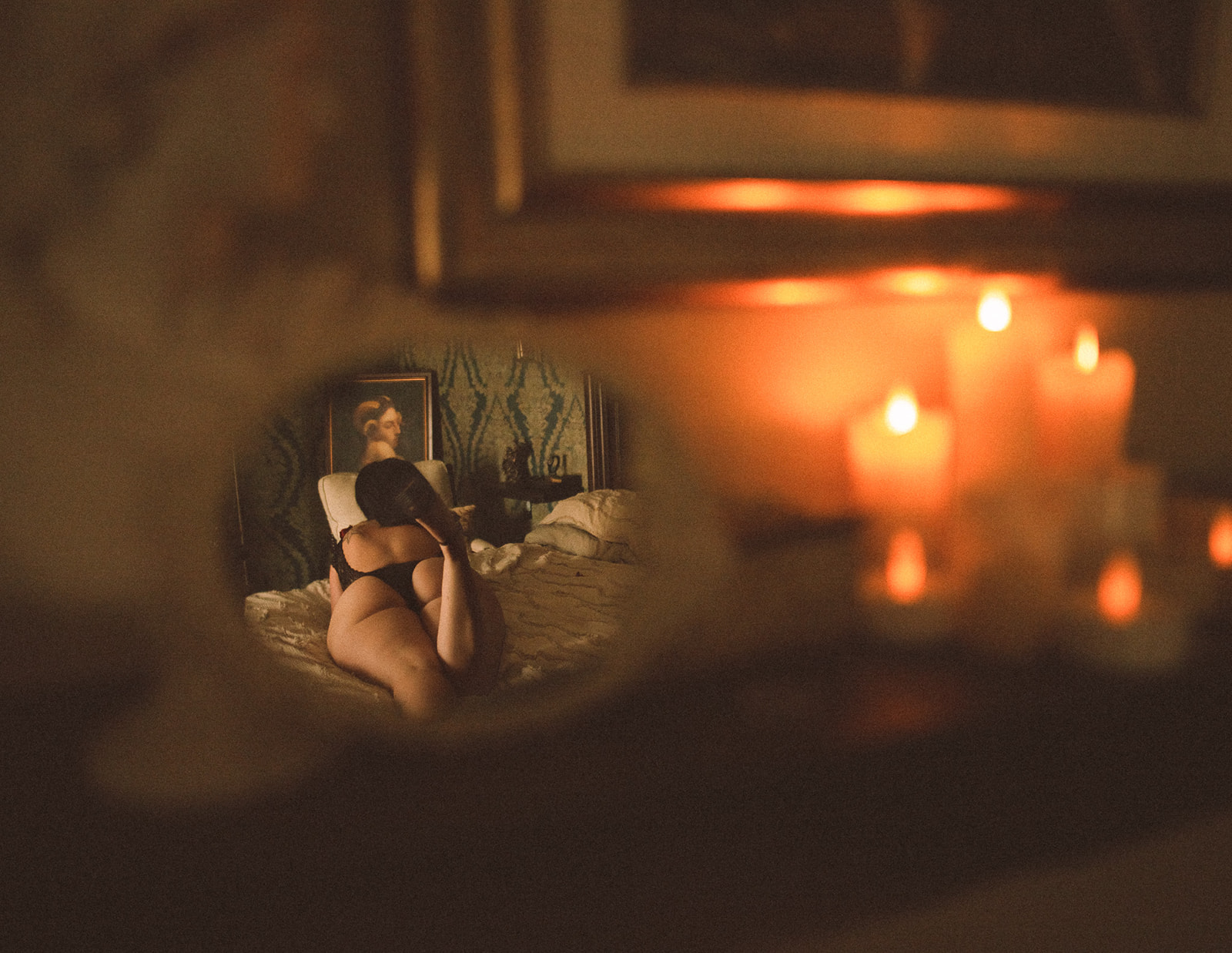 A peak in a mirror on a dresser with candles of a woman laying across a bed in black lingerie after laser hair removal in Helena, MT
