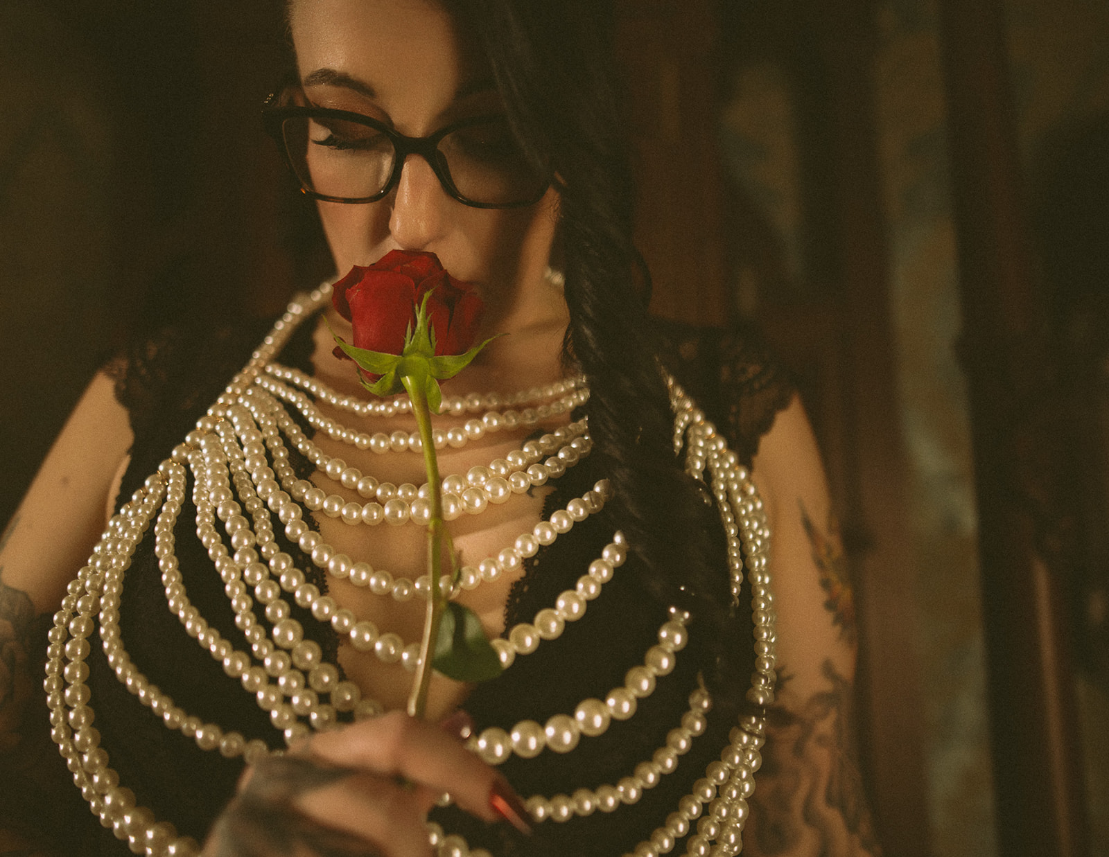 A woman smells a red rose while standing in a bedroom in black lace