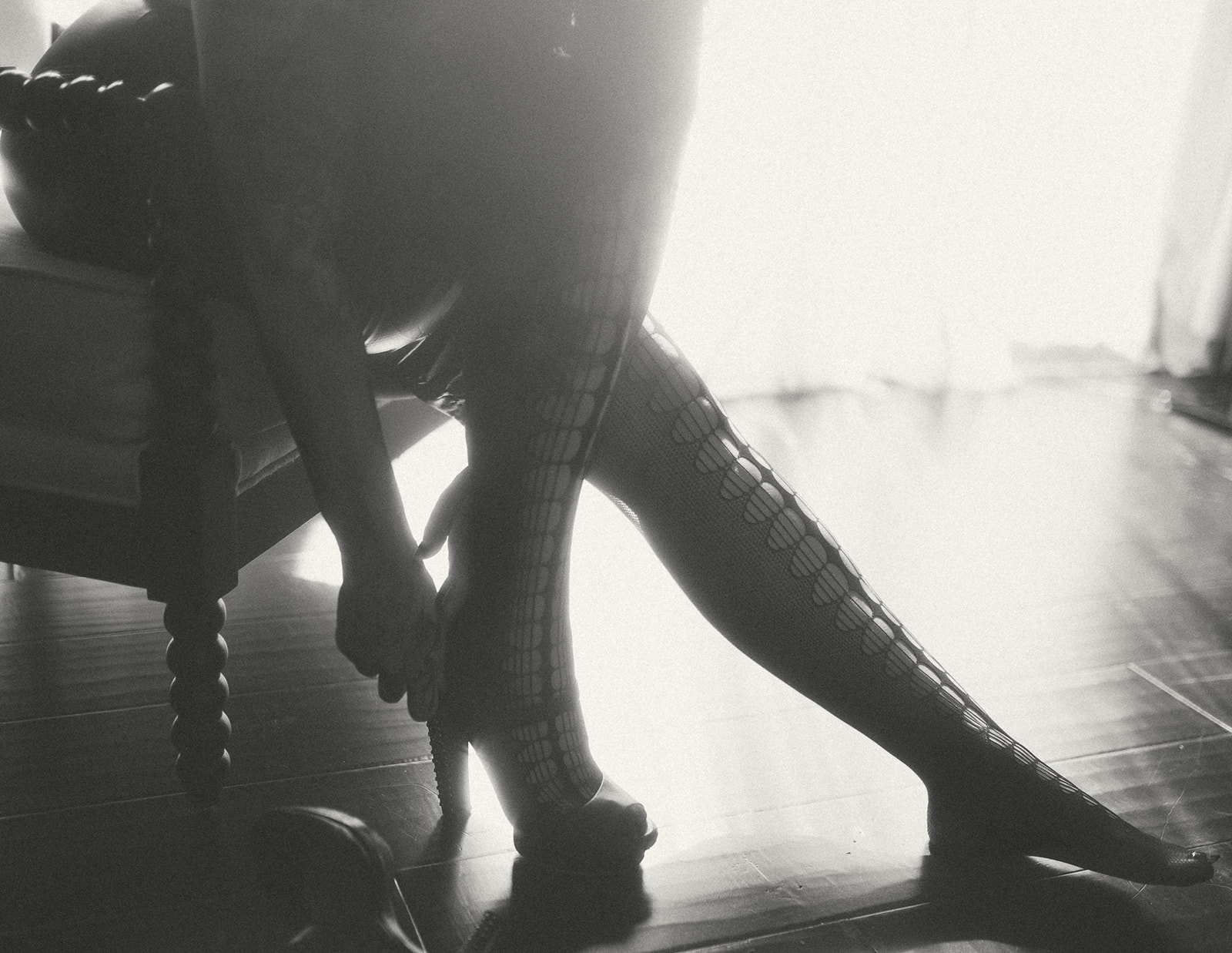 A woman puts on her high heels over her fishnets while sitting in a chair in a window after visiting The Exotic Peach