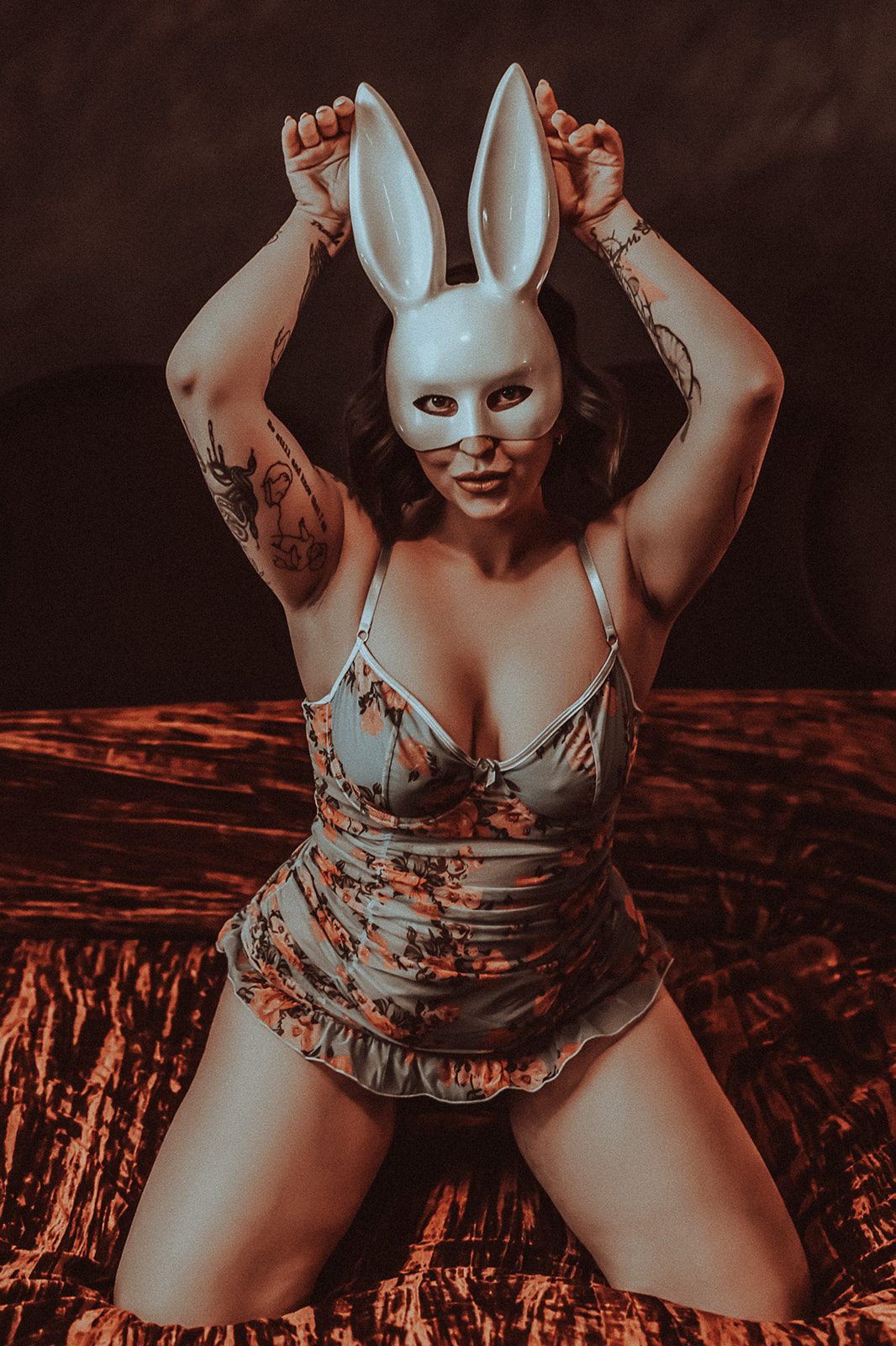 A woman kneels on a bed in pajamas while wearing a bunny mask