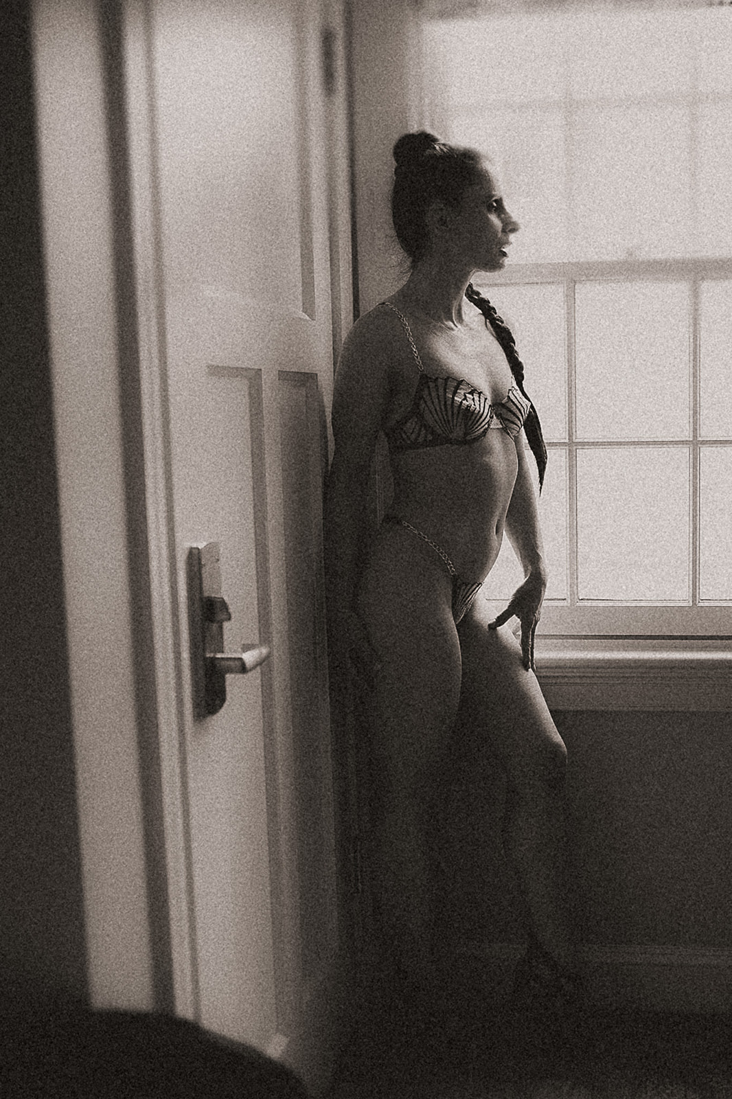 A woman in her underwear with a long braid stands in a window after finding great botox in Missoula