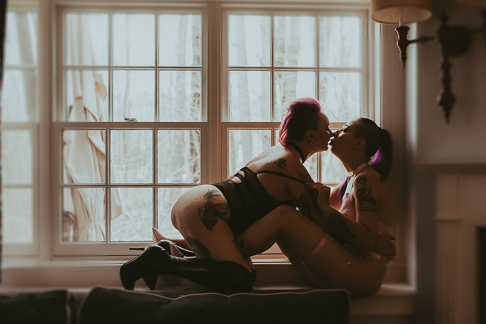 Women lean in for a kiss while sitting in a window sill in lingerie