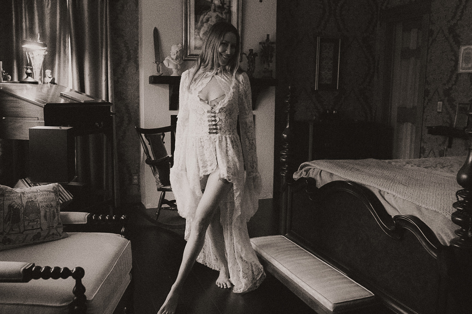 A look at a woman walking in an antique filled bedroom in a lace dress with a smile