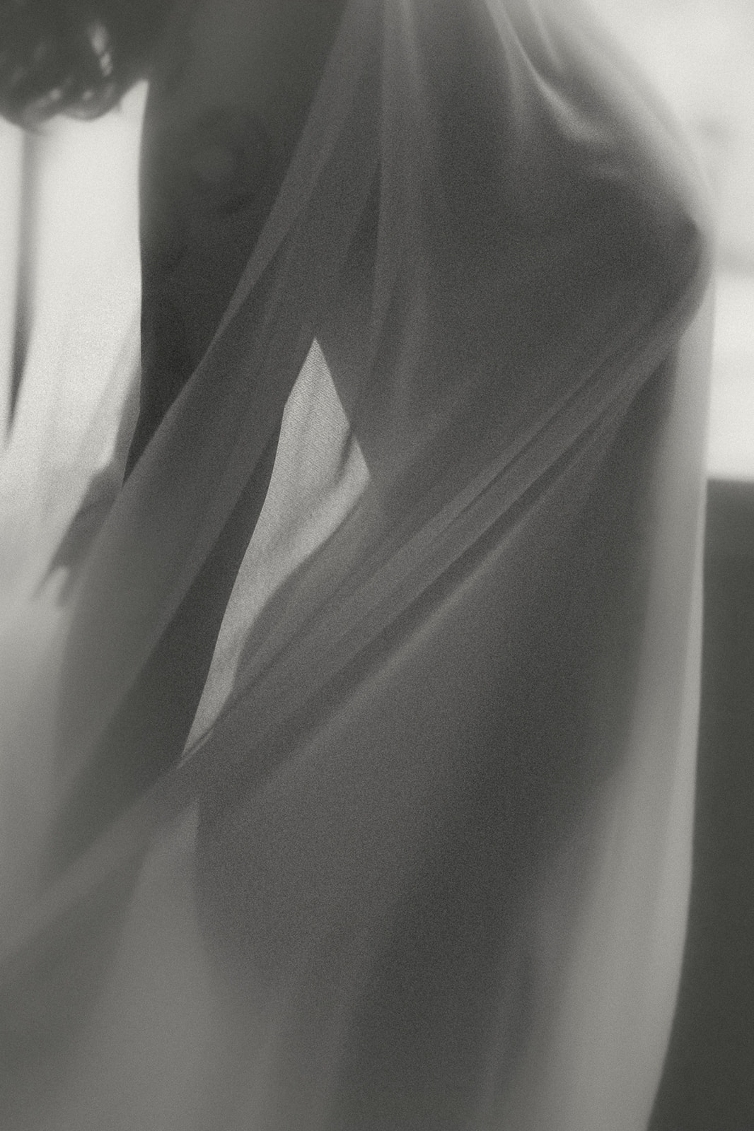 Details of a woman's body in black and white hiding behind a sheer sheet