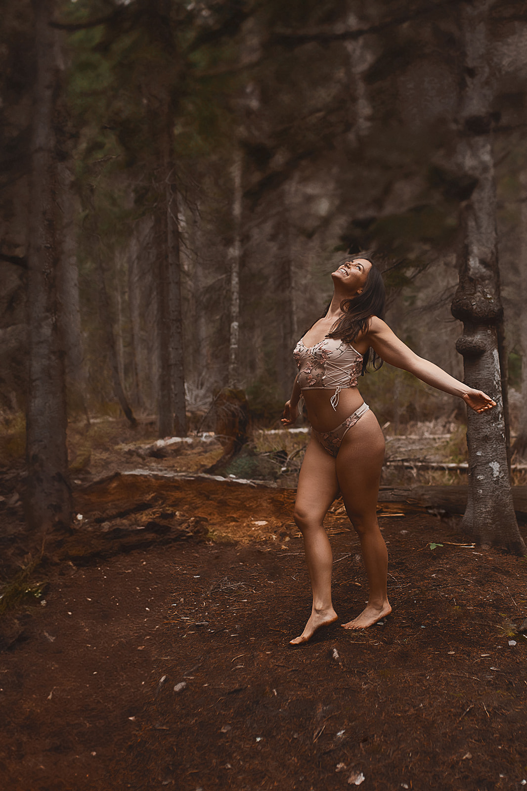 A woman in a white coreset and matching underwear dances happily in a forest with arms open after finding microblading in Missoula
