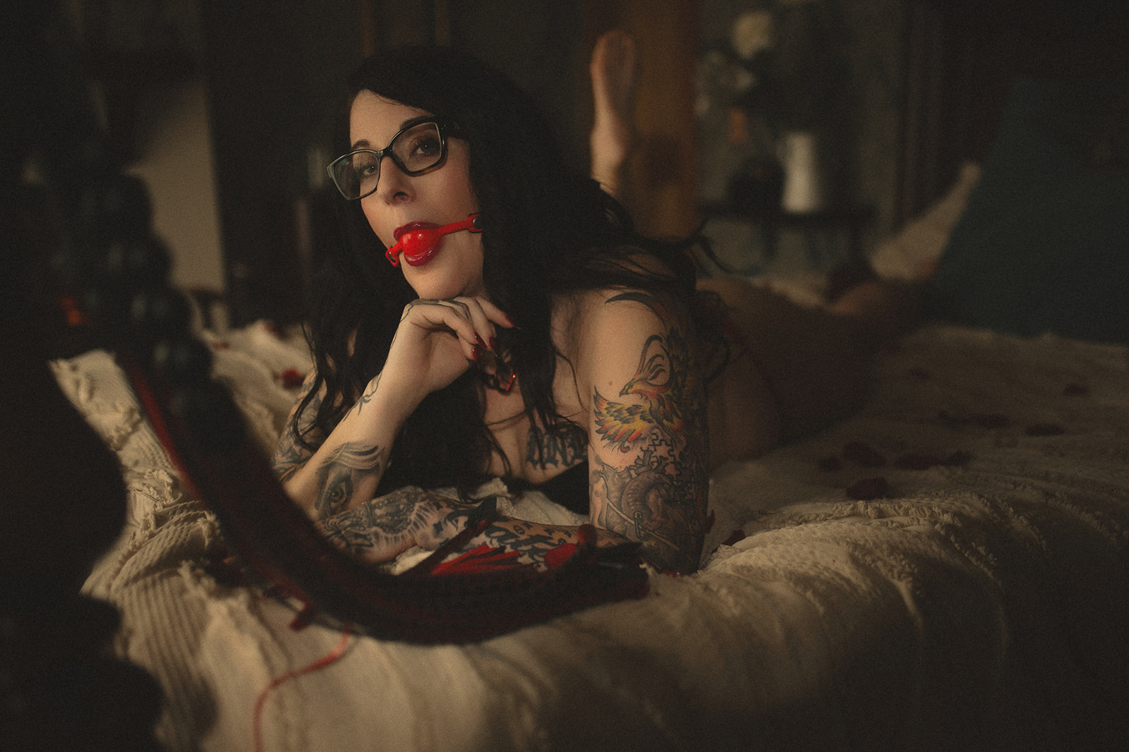 A woman wearing a red ball gag lays across a bed aafter enjoying waxing in Missoula