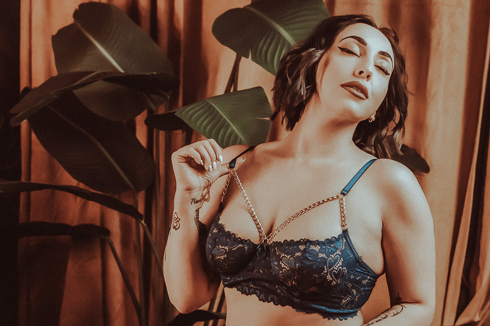 A woman stands in a window while pulling on her black lace bra strap in a studio