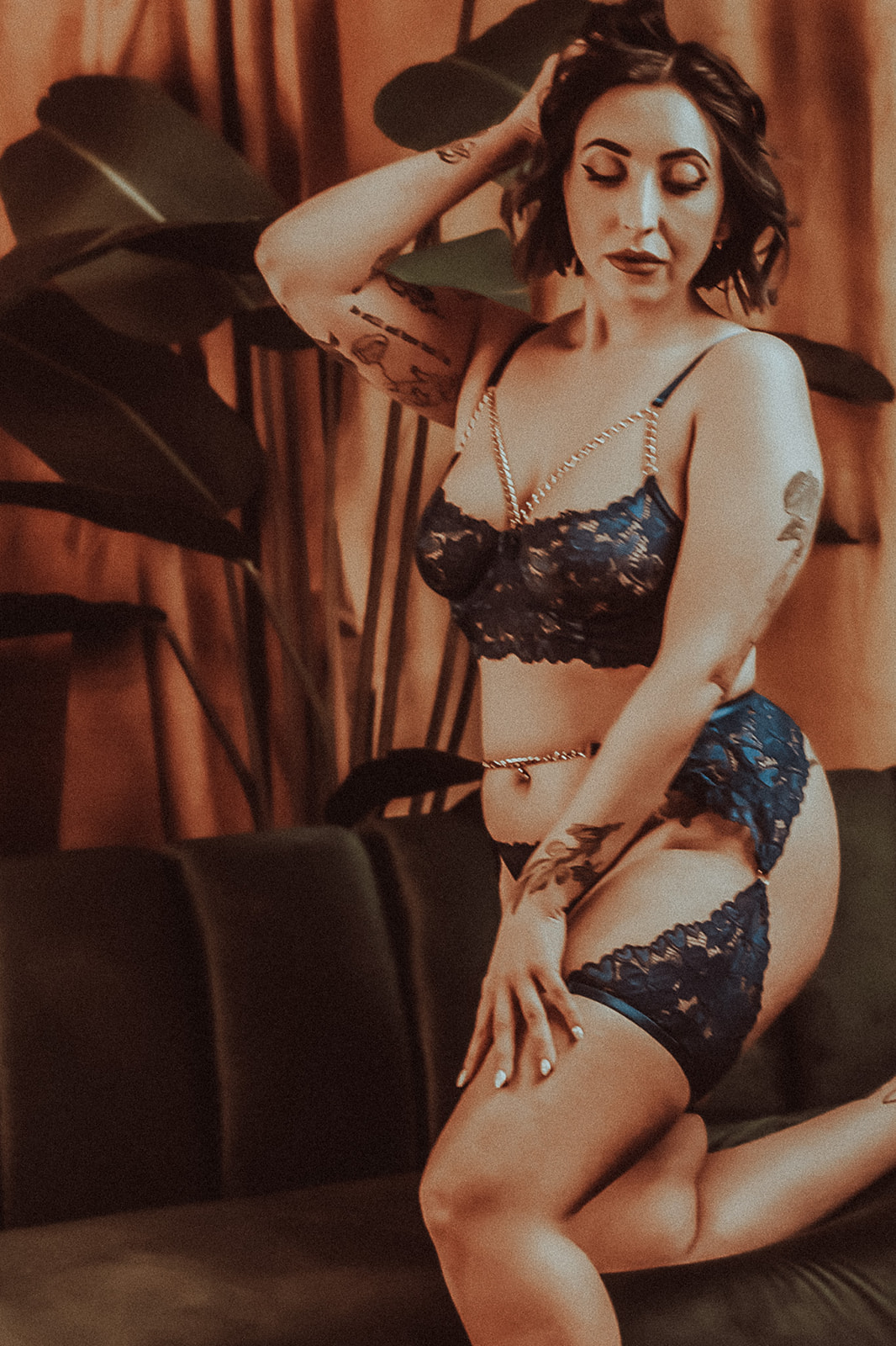 A woman in lace lingerie with gold straps kneels on a leather couch with a hand in her hair after some hot yoga in Kalispell