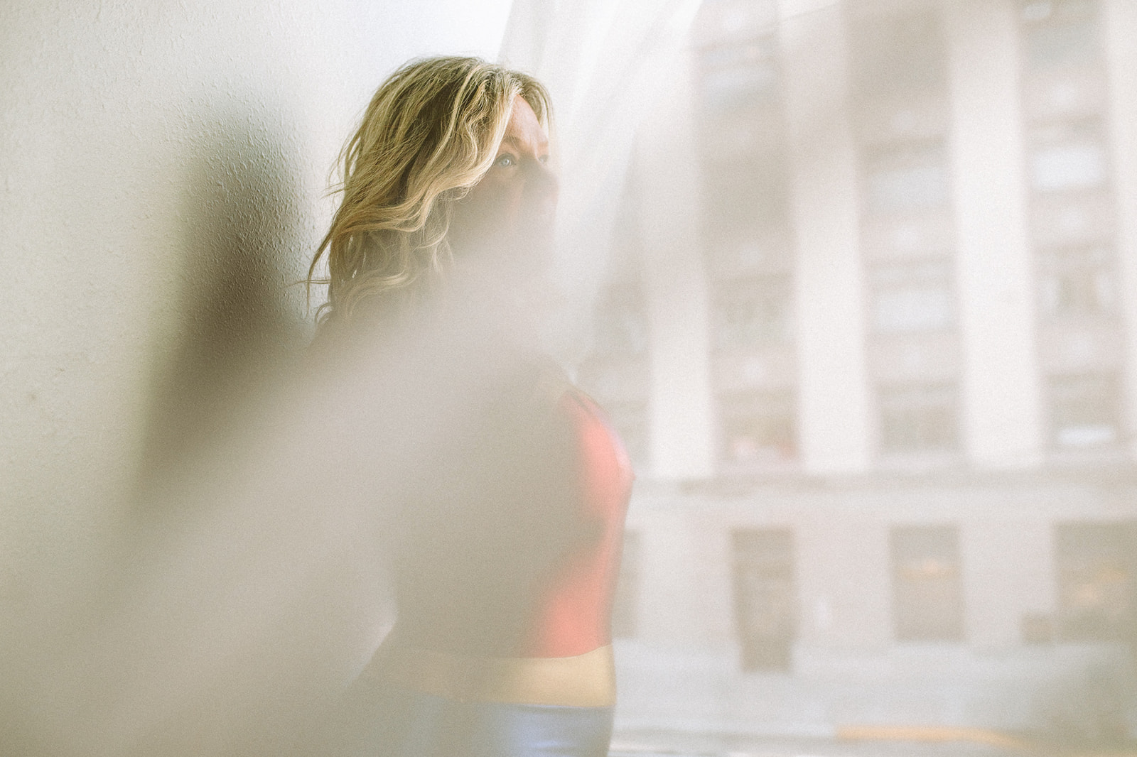 A look through a curtain of a woman standing in a window in a wonder woman costume